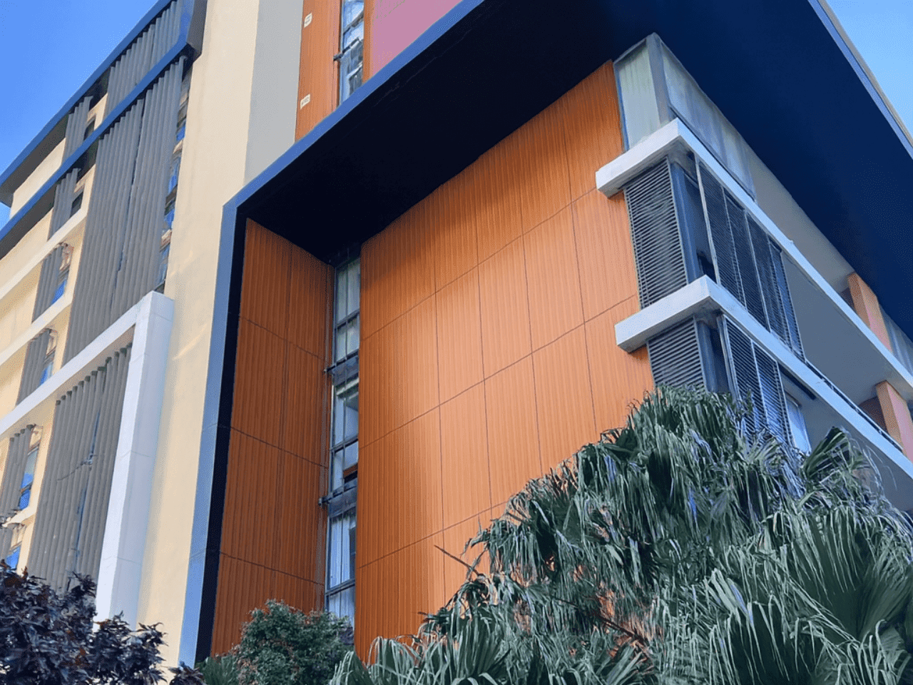 Modern multi-residential building featuring ALPOLIC™ NC/A1 non-combustible mineral core aluminium cladding in timber pattern finish framed by palm trees